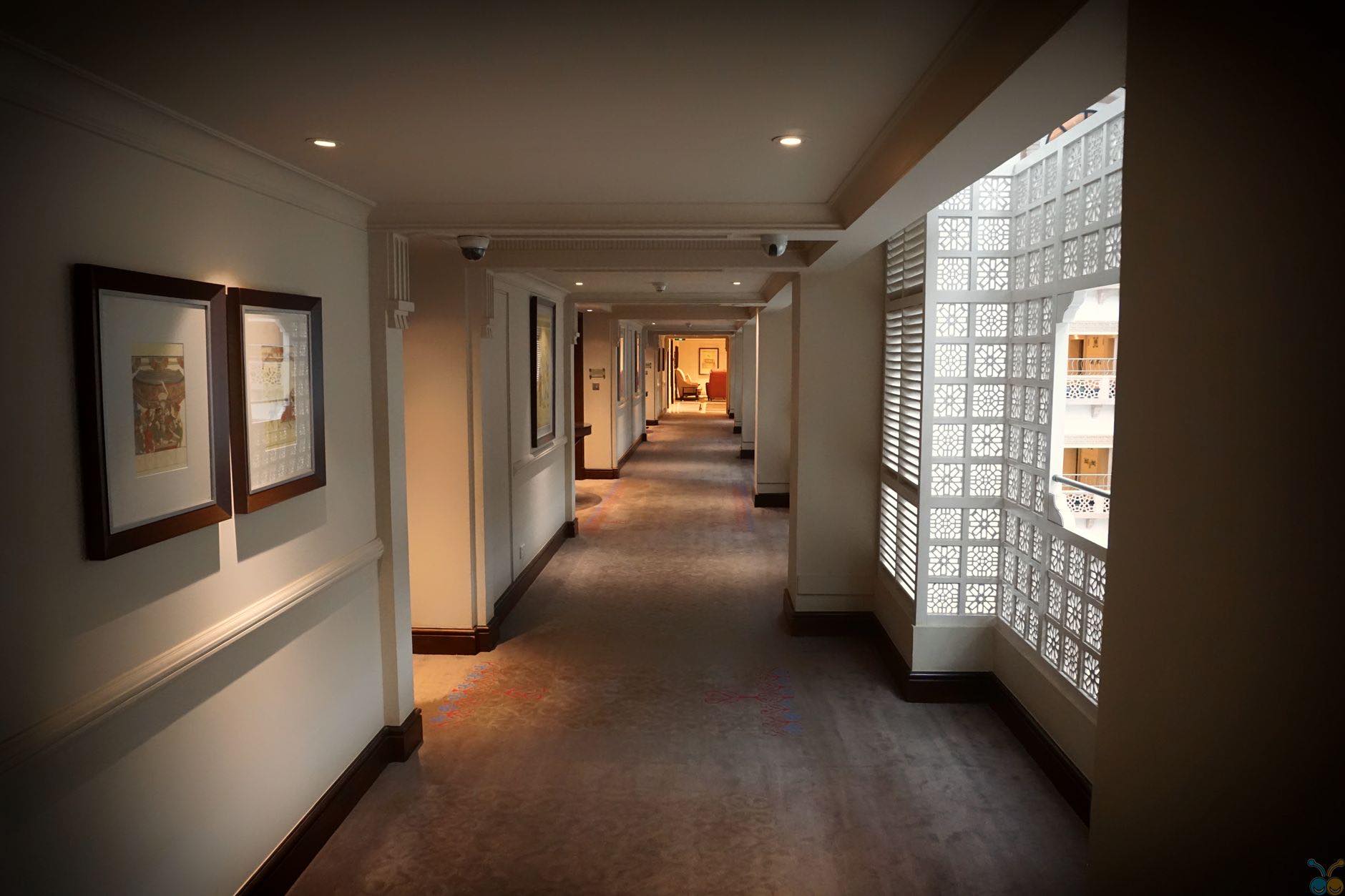 A dim corridor with framed pictures on one wall and a lit glass block panel on the other