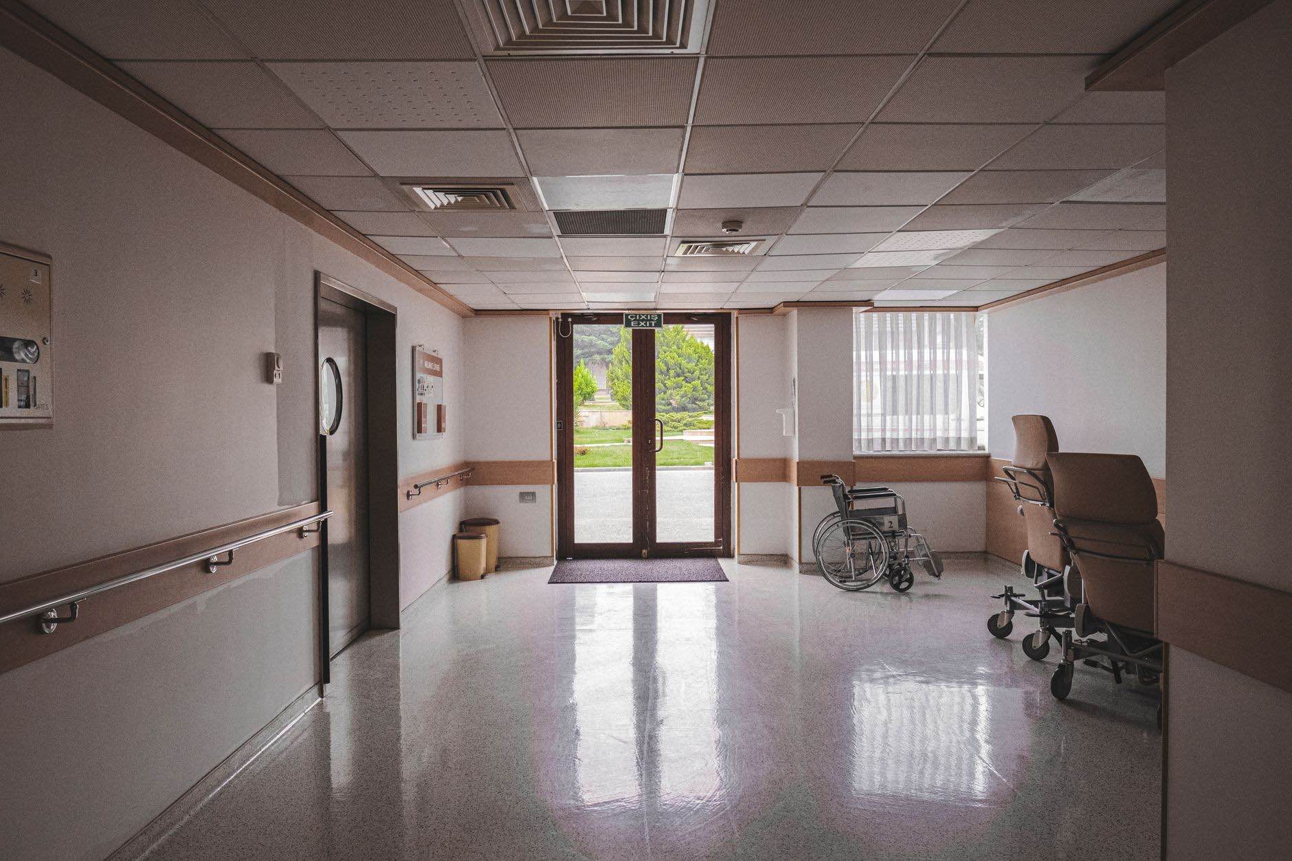 A clinical corridor with a handrail along the wall and daylight at the far doors