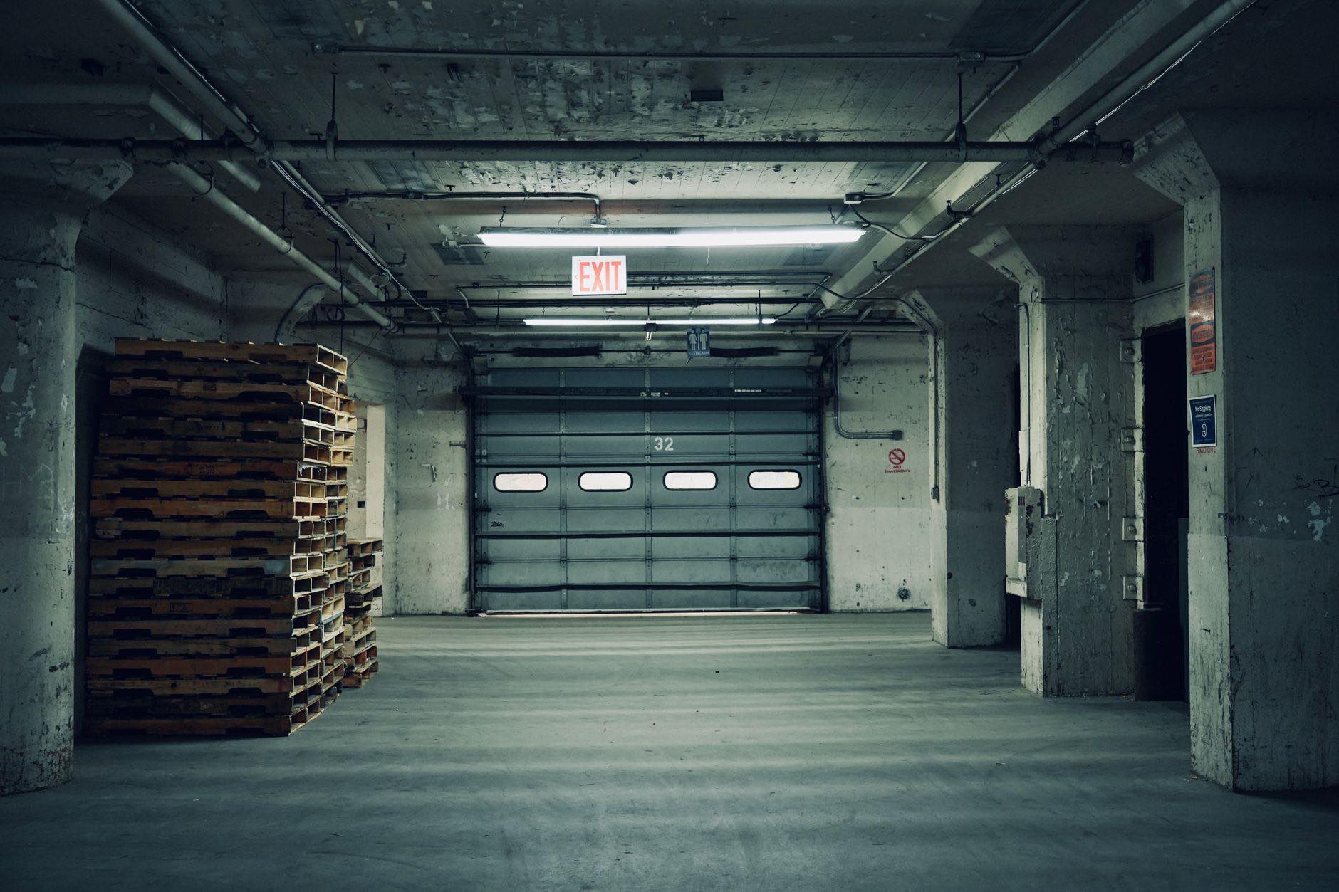 A covered loading bay inside a building, with stacked pallets and a shutter door at the end