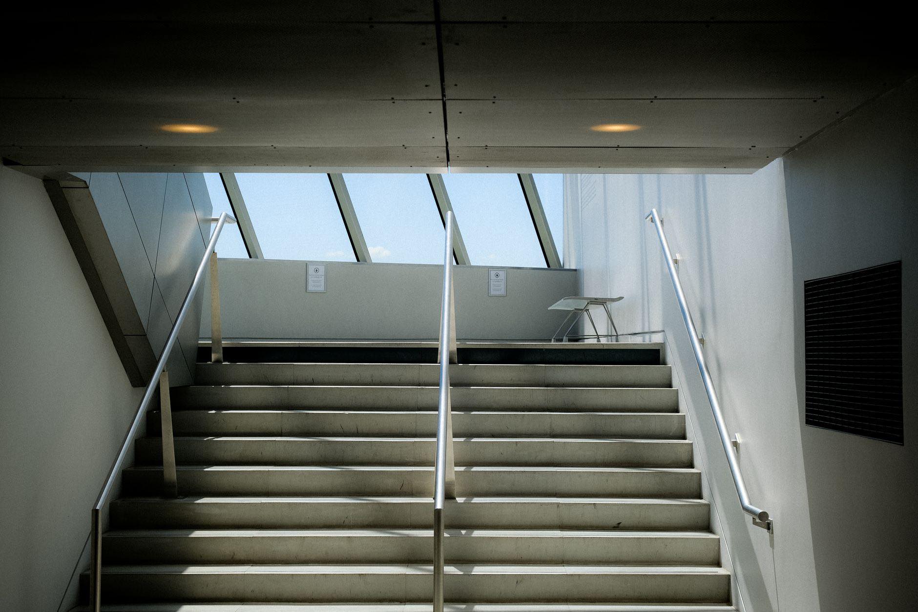 A concrete staircase lit from a skylight above the landing
