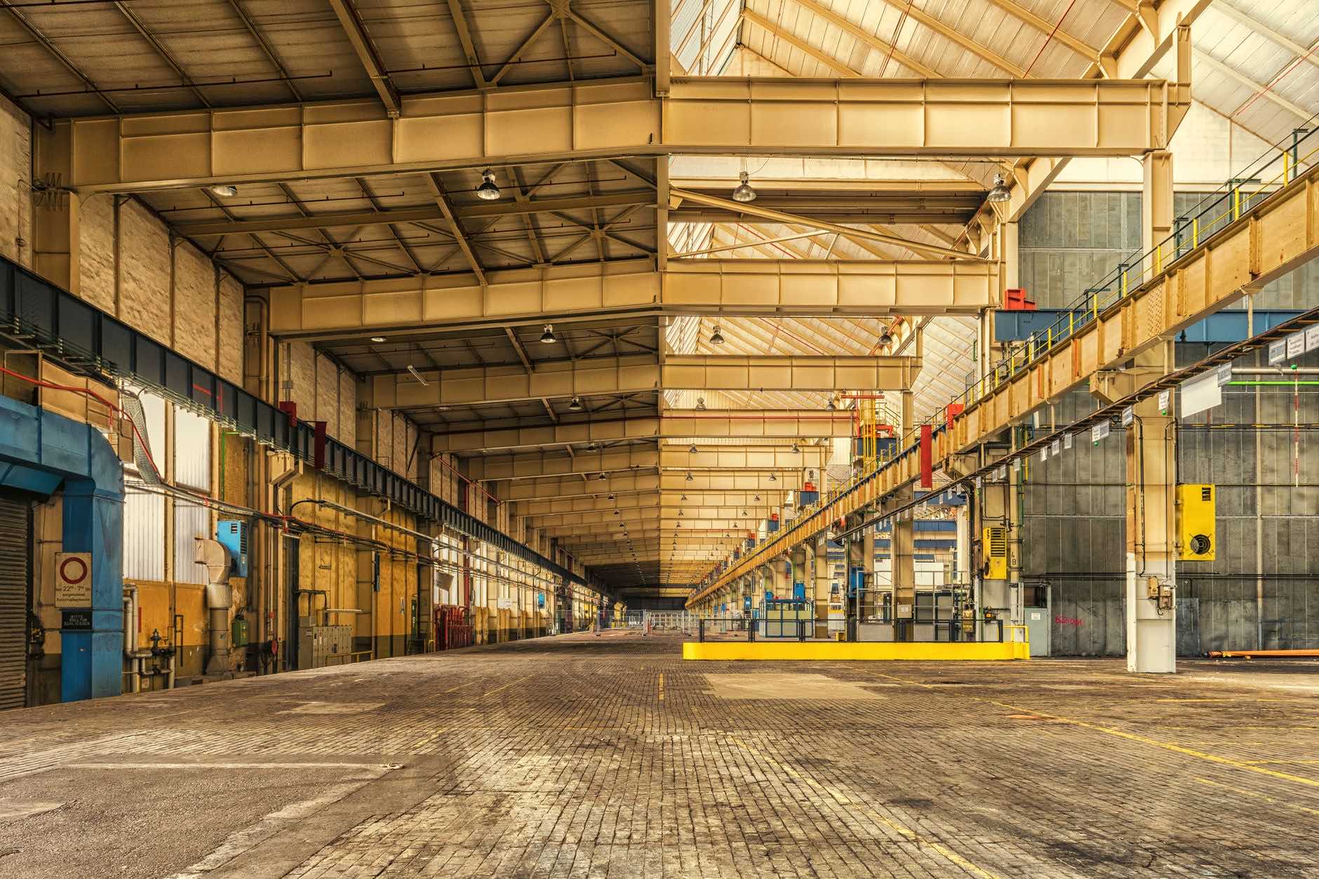 A long empty industrial hall with a steel roof structure and a brick floor
